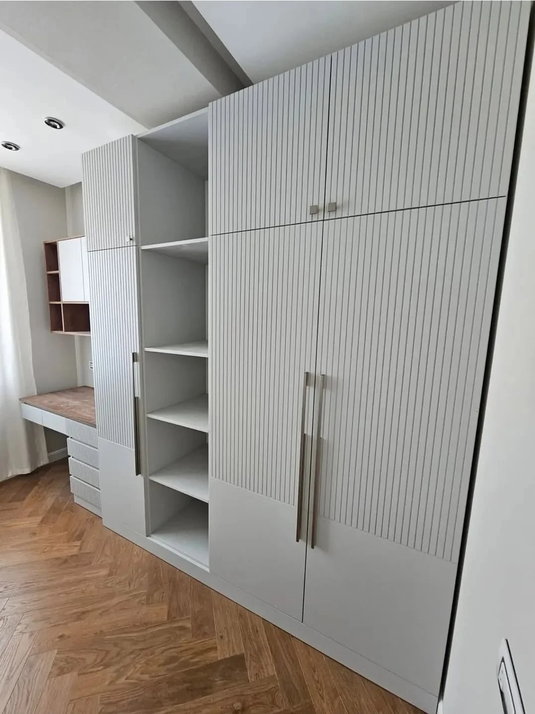 Çizgili kapaklı gardırop. Dikey çizgili kapaklar, ortadaki açık raflar ve yandaki çalışma yüzeyi aynı dolap düzeninde görülüyor.
